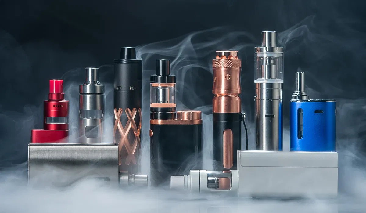 Verschiedene Vape-Geräte in einer Reihe, umgeben von Rauch