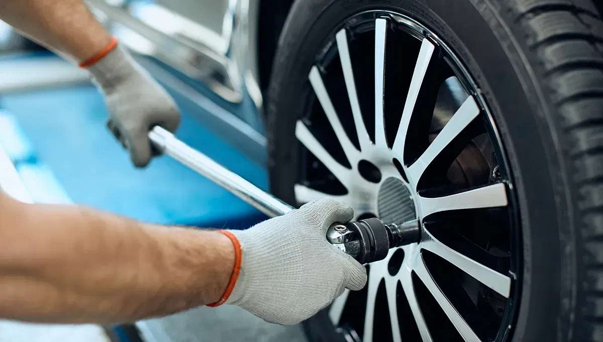 Automechaniker, der mithilfe eines Drehmomentschlüssels die Radschrauben eines Autos anzieht Automechaniker, der mithilfe eines Drehmomentschlüssels die Radschrauben eines Autos anzieht