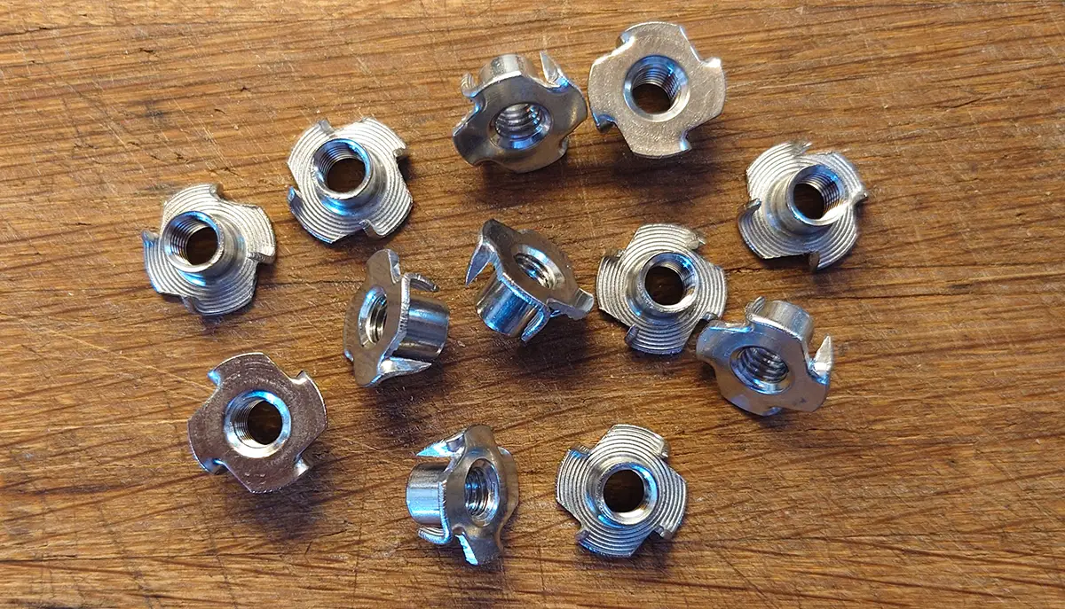 Twelve identical metal wood thread inserts are lined up next to each other on a wooden table. Twelve identical metal wood thread inserts are lined up next to each other on a wooden table.
